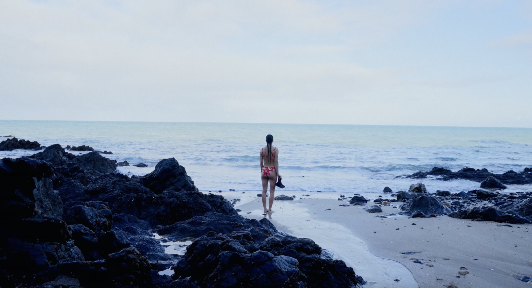 A swimmer seen from behind facing the sea, on the rocky shore