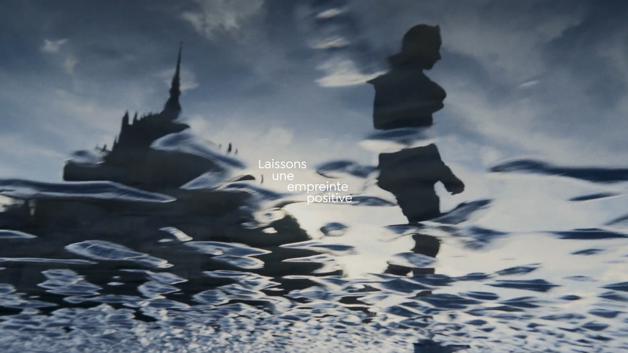 Reflection in the water of Mont-Saint-Michel and a silhouette, with the text « Laissons une empreinte positive »
