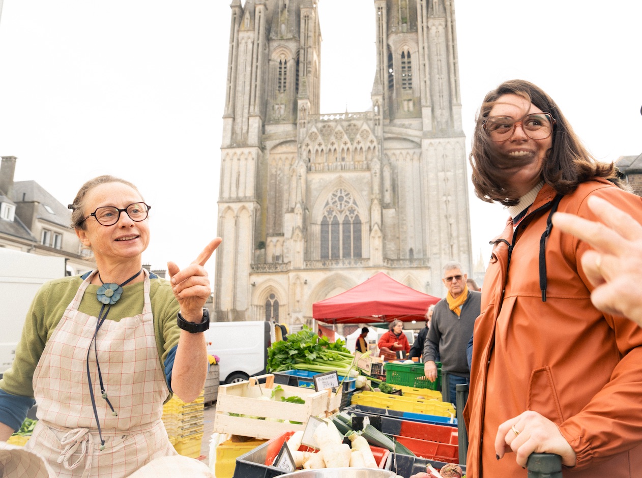 Two visitors at a market in front of Coutances Cathedral