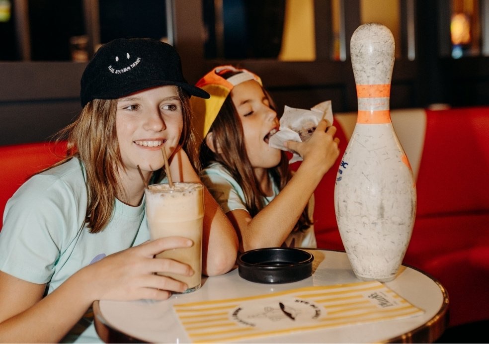 Two children sharing a milkshake at a bowling alley